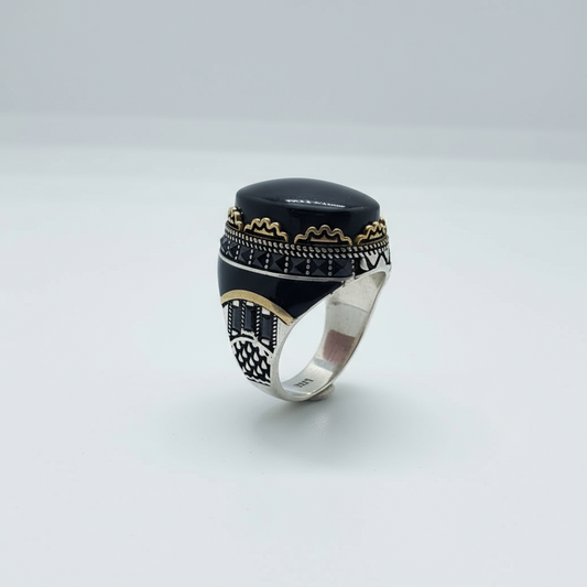 Silver ring with black stone and gold accents on a light gray background